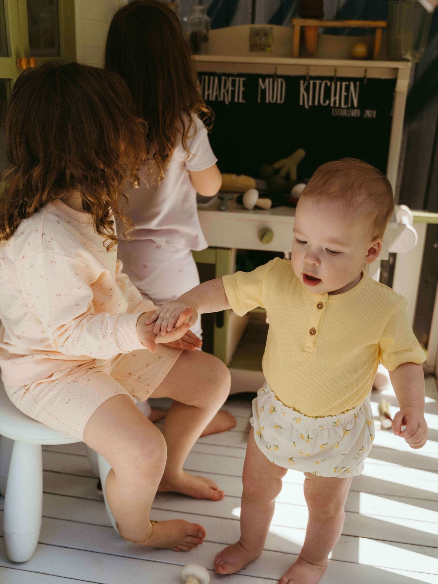 Two children playing on a wooden floor with a play kitchen in the background.