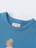 Close-up of a blue t-shirt collar with a small printed graphic below Axel Short Sleeve Tee - Milo Biking Boys