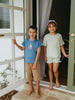 Two children standing on a porch with a white door and window in the background. Axel Short Sleeve Tee - Milo Biking Boys