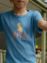 Child wearing a blue t-shirt with a graphic of a person on a bicycle. Axel Short Sleeve Tee - Milo Biking Boys