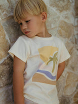 Child wearing a t-shirt with a palm tree design against a stone wall. Axel Short Sleeve Tee - Palm Beach Boys