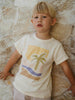 Child wearing a t-shirt with a palm tree design against a stone wall. Axel Short Sleeve Tee - Palm Beach Boys