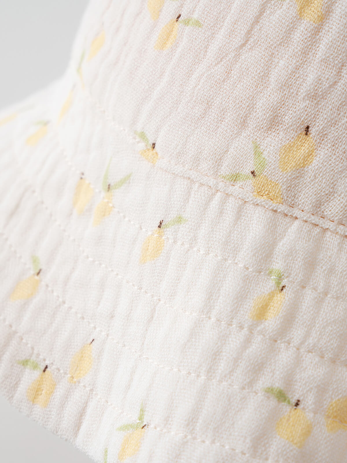 Close-up of white textured fabric with yellow lemon and green leaf pattern Baby Bucket Hat - Lemons Baby girl