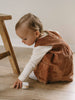 Child in a brown corduroy dress sitting on a wooden floor. Baby Corduroy Dress - Russet Baby girl