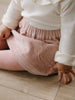 Person wearing a white top and pink ribbed pants sitting on a wooden floor. Baby Corduroy Skirt - Blush Baby girl