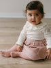 Child wearing a white top with ruffled collar and pink skirt sitting on a wooden floor. Baby Corduroy Skirt - Blush Baby girl