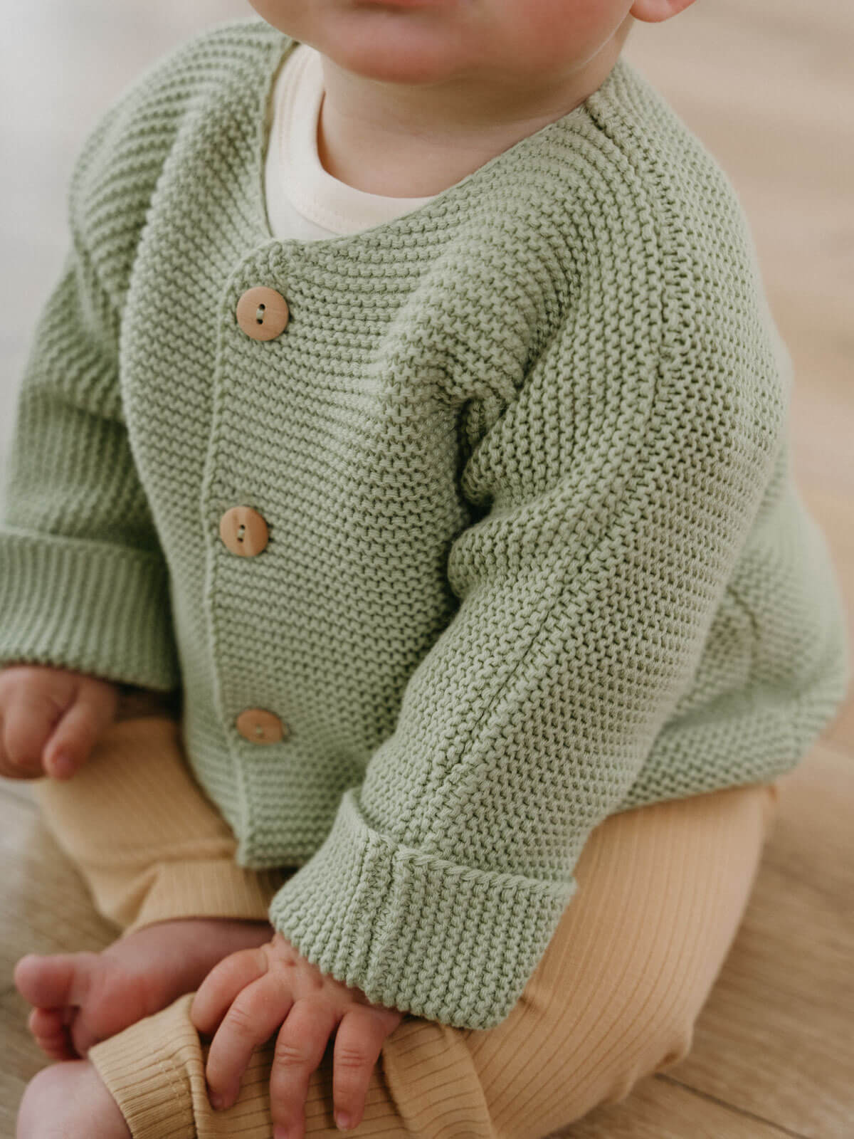 Child wearing a green knitted cardigan with brown buttons on a neutral background Baby Cotton Cardigan - Sage Baby boy