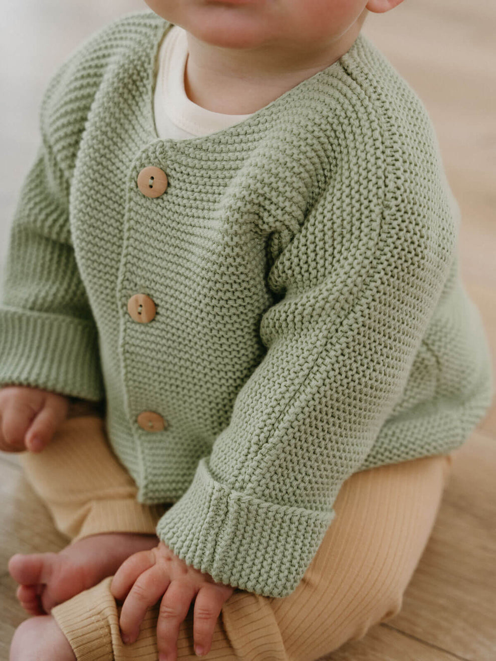 Child wearing a green knitted cardigan with brown buttons on a neutral background Baby Cotton Cardigan - Sage Baby boy