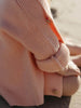 A close-up of a child wearing a soft peach knit cardigan, with the sleeve rolled up and a small wooden button visible, in an outdoor setting.