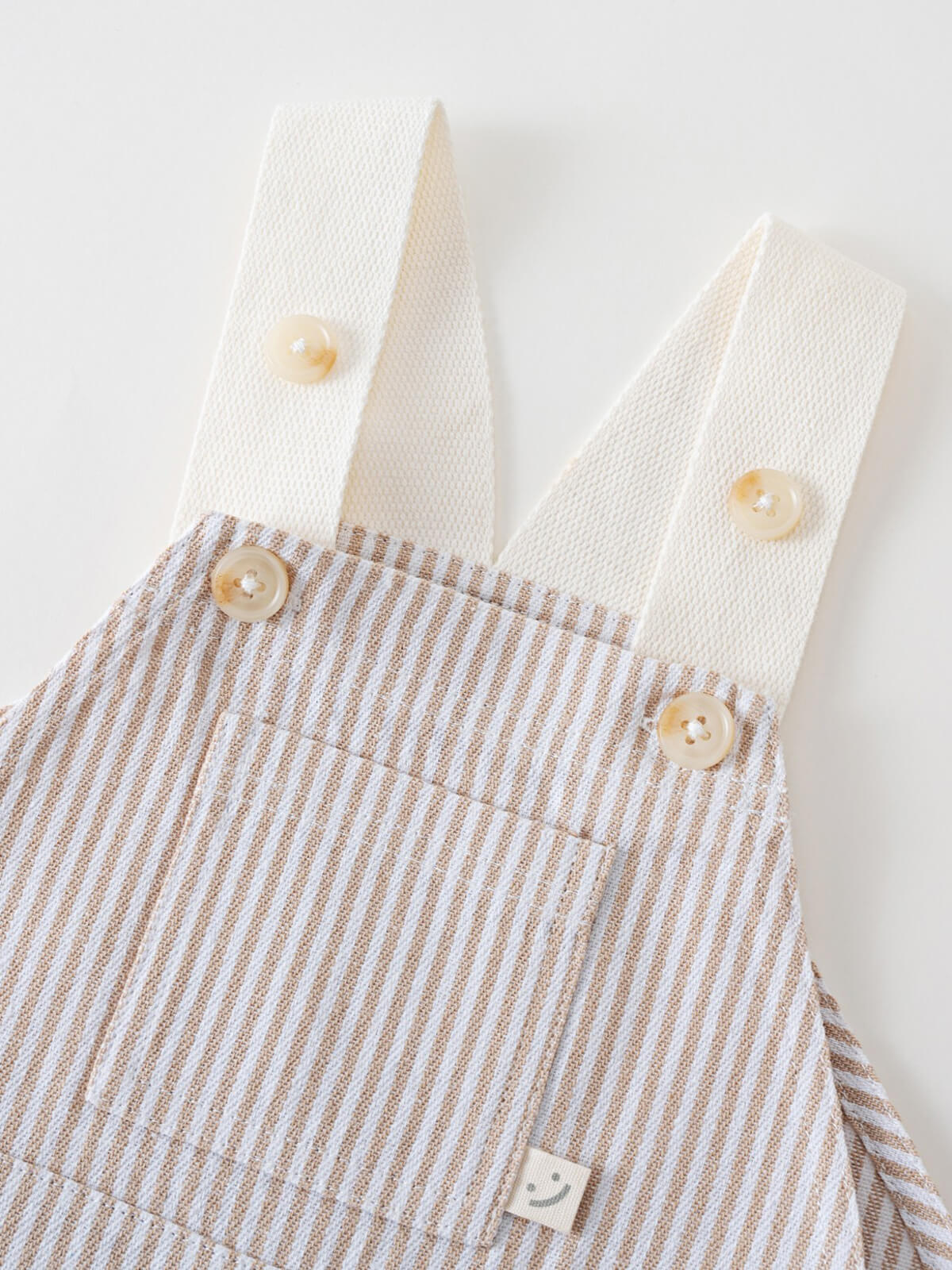 Close-up of striped dungarees with white straps and cream buttons Baby Dungarees - Sand Stripe Baby boy