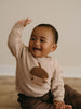Baby in beige sweater with acorn design waving and smiling on wooden surface Baby Feature Print Jumper - Little Acorn Baby boy