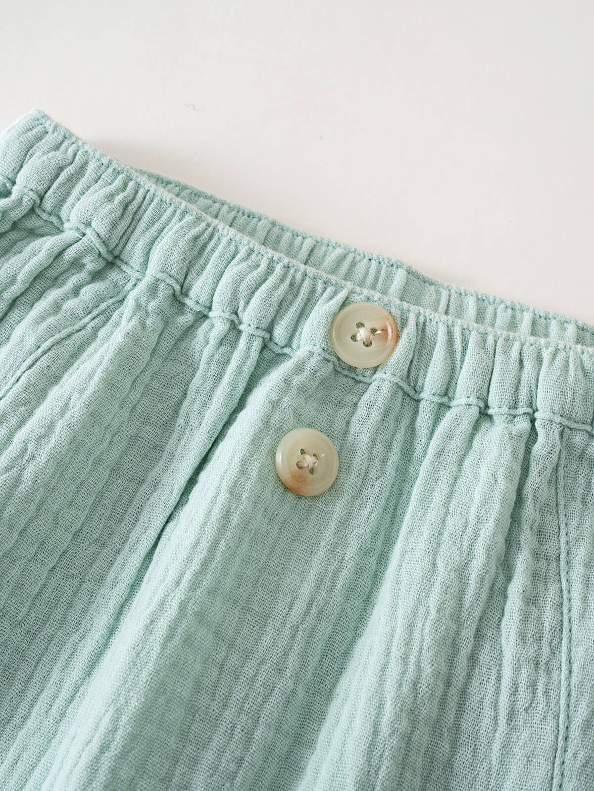 Close-up of mint green textured fabric pants with elastic waistband and buttons Baby Muslin Pants - Calla Green Baby boy