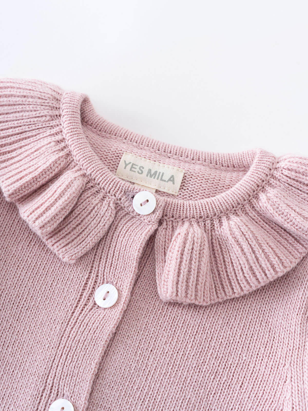 Pink knitted cardigan with ruffled collar and 'YES MILA' label on a light gray background