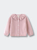 Pink knitted cardigan with ruffled collar on a light gray background
