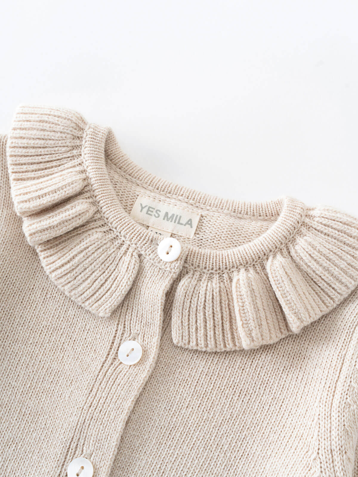 Beige knitted cardigan with ruffled collar and visible brand label on a light background