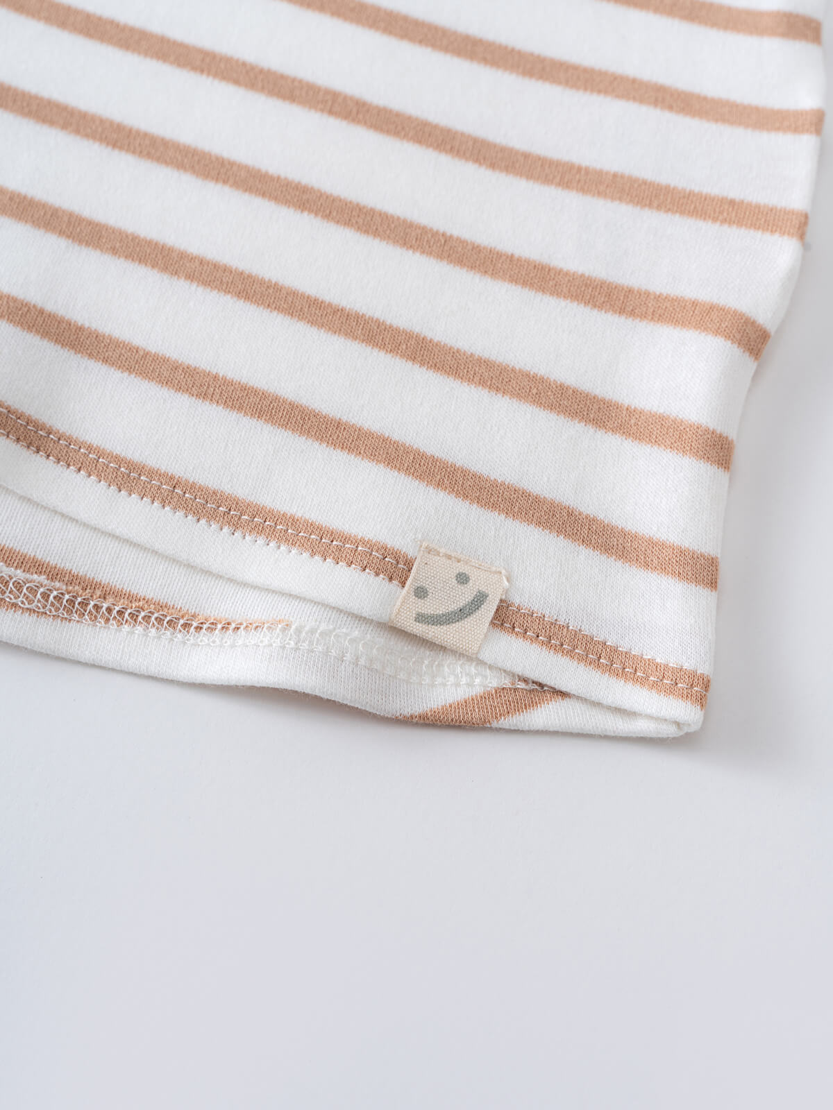 Close-up of a striped fabric hem with a small smiley face label baby Sleeveless Tee - Sand Stripe Baby boy