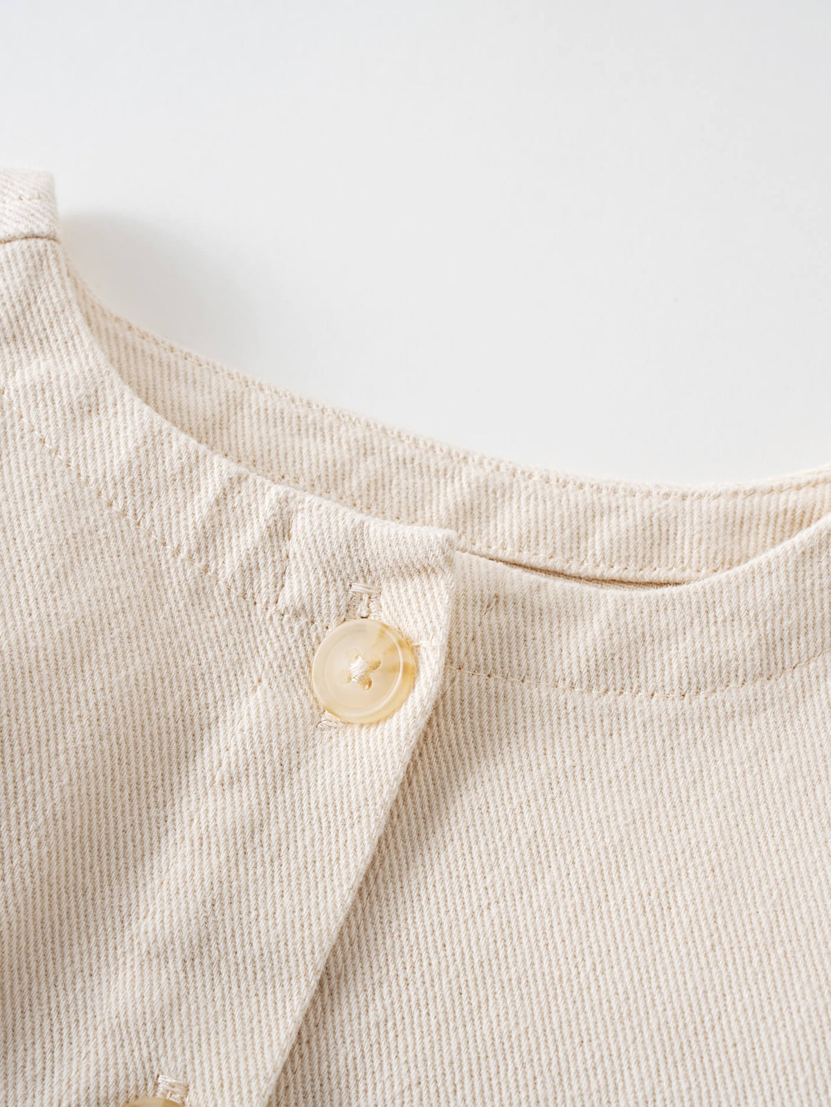 Close-up of a cream textured fabric collar with a pale button detail Baby Twill Jacket - Salt Baby 