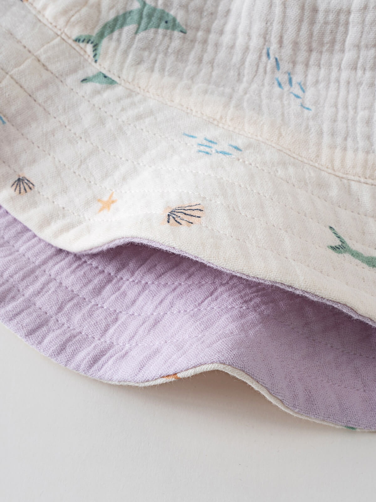 Close-up of white fabric with dolphin and sea life pattern, lavender reverse side Bucket Hat - Dolphin Fun Girls