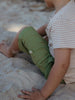 A child sitting on sandy ground wearing olive green cargo shorts and a cream and brown striped t-shirt.
