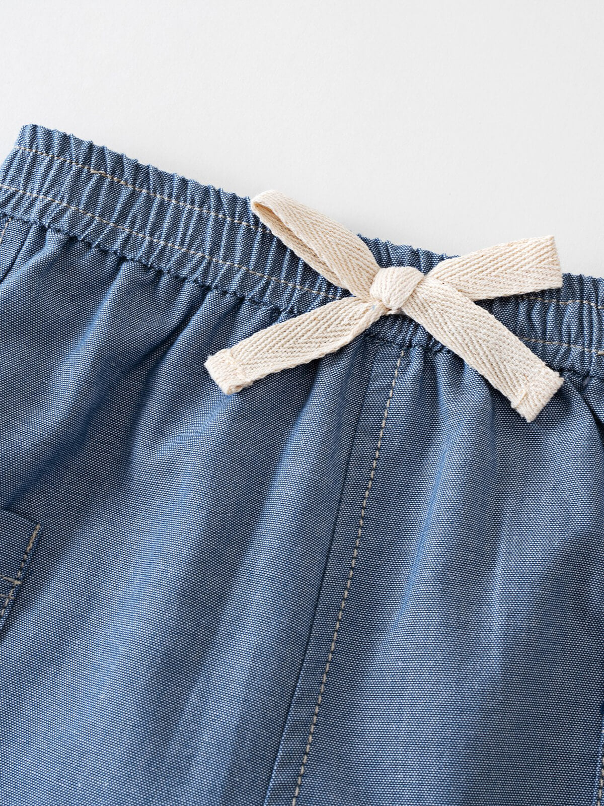 Close-up of blue chambray shorts with cream ribbon bow at waistband Chambray Shorts - Blue Chambray Baby boy