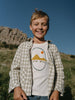 Child wearing a 'Stay Wild' t-shirt in a natural setting with mountains. Check Shirt - Brushed Cotton Check Boys
