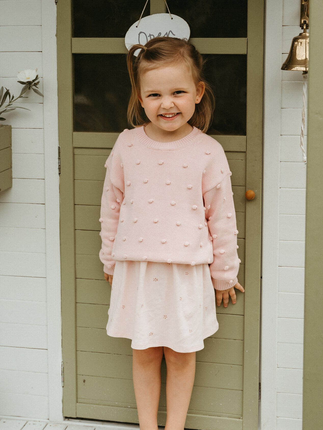 Young girl in a pink outfit standing in front of a door.