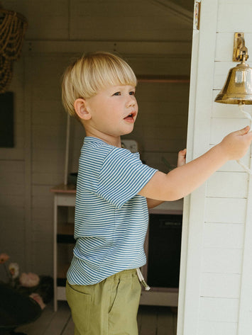 Young boy ringing a doorbell inside a house. Cooper Henley Tee - Blue Stripe Boys