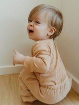 Child in a beige outfit sitting on the floor against a plain wall