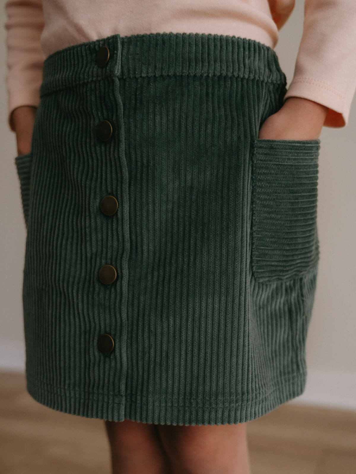 Green corduroy skirt with buttons on a neutral background