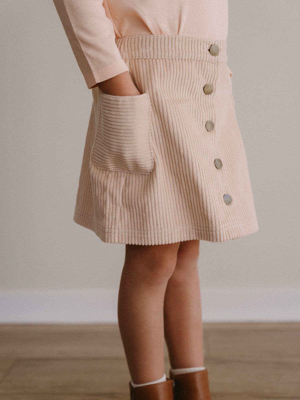 Beige corduroy skirt with button details worn by a person, on a plain background Corduroy Skirt - Clay Girls