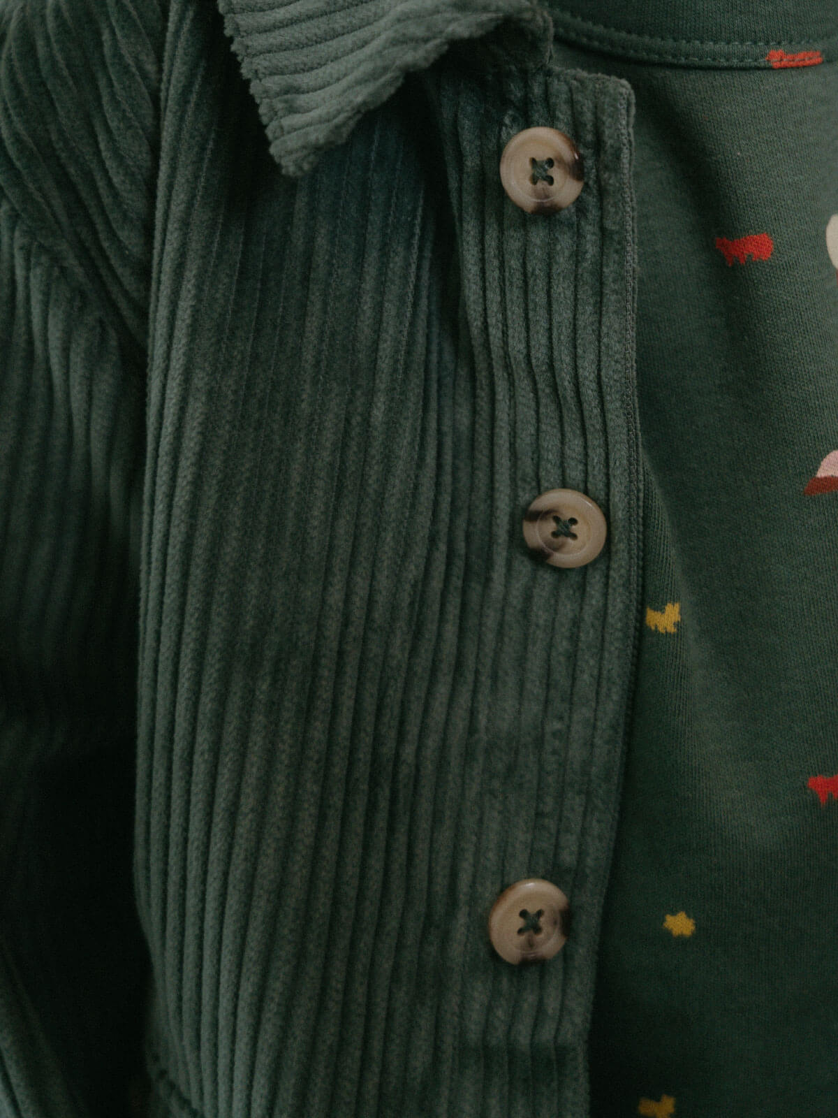 Close-up of a green corduroy jacket with buttons and a patterned background Corduroy Jacket - Balsam Girls and Boys