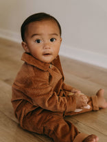 Baby wearing a brown corduroy outfit sitting on a wooden floor. Corduroy Jumpsuit - Russet Baby boy