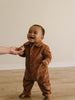 Baby in a brown corduroy outfit standing on a wooden floor with a blurred background Corduroy Jumpsuit - Russet Baby boy
