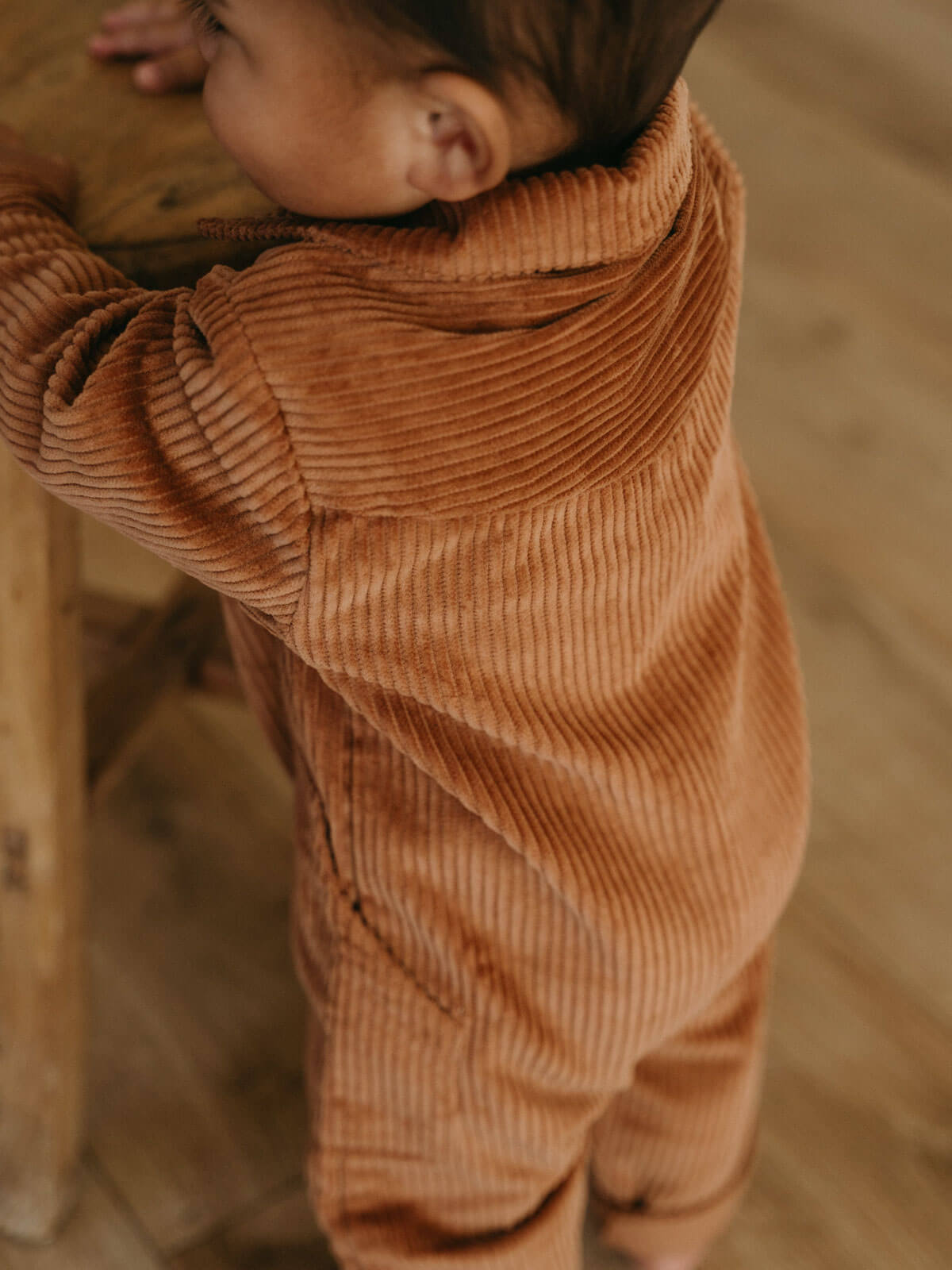 Child wearing brown corduroy pants standing on a wooden floor. Corduroy Jumpsuit - Russet Baby boy