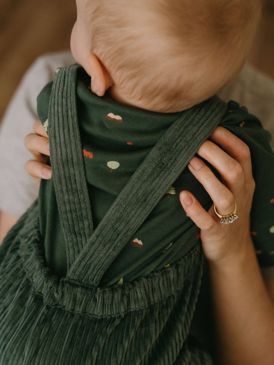 Person holding a baby wrapped in a green wrap with a blurred background Corduroy Overalls - Balsam Baby boy