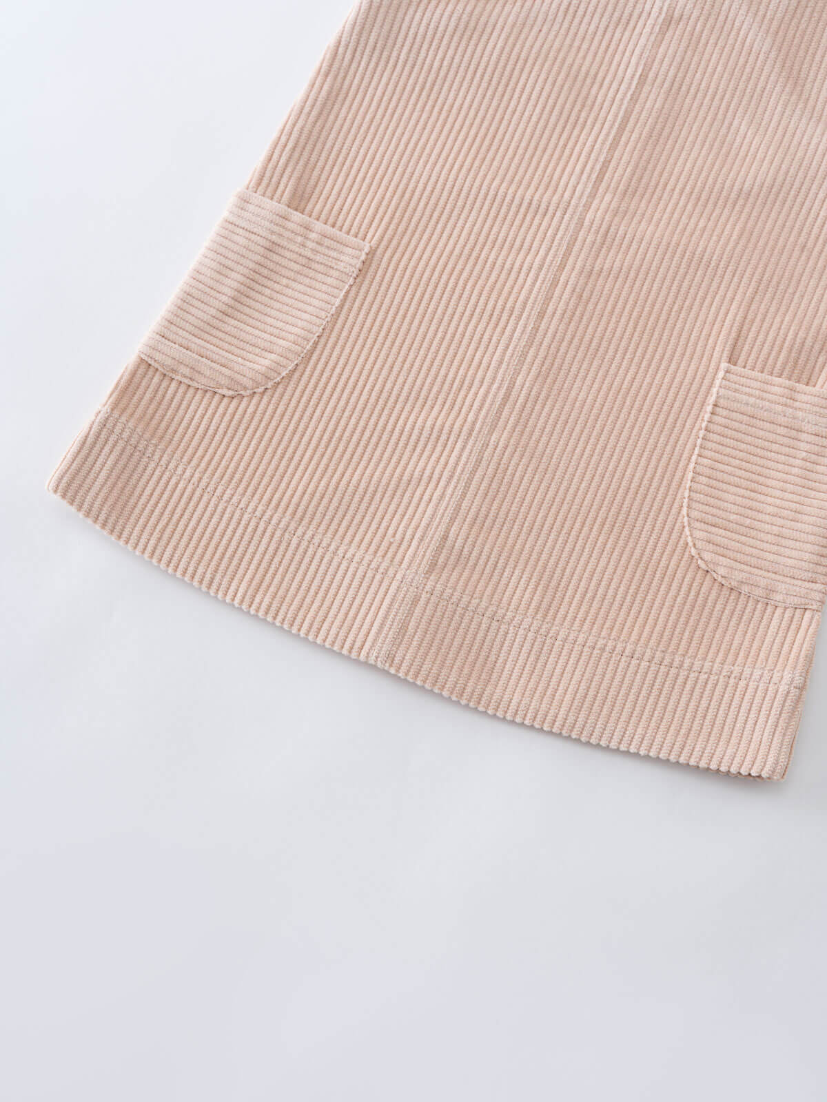 Close-up of a beige corduroy pinafore dress with two front pockets on a light gray background Corduroy Pinafore Dress - Clay Girls