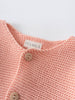 Close-up of a coral pink knitted cardigan with wooden buttons and label Cotton Cardigan - Toasted Peach Baby girl