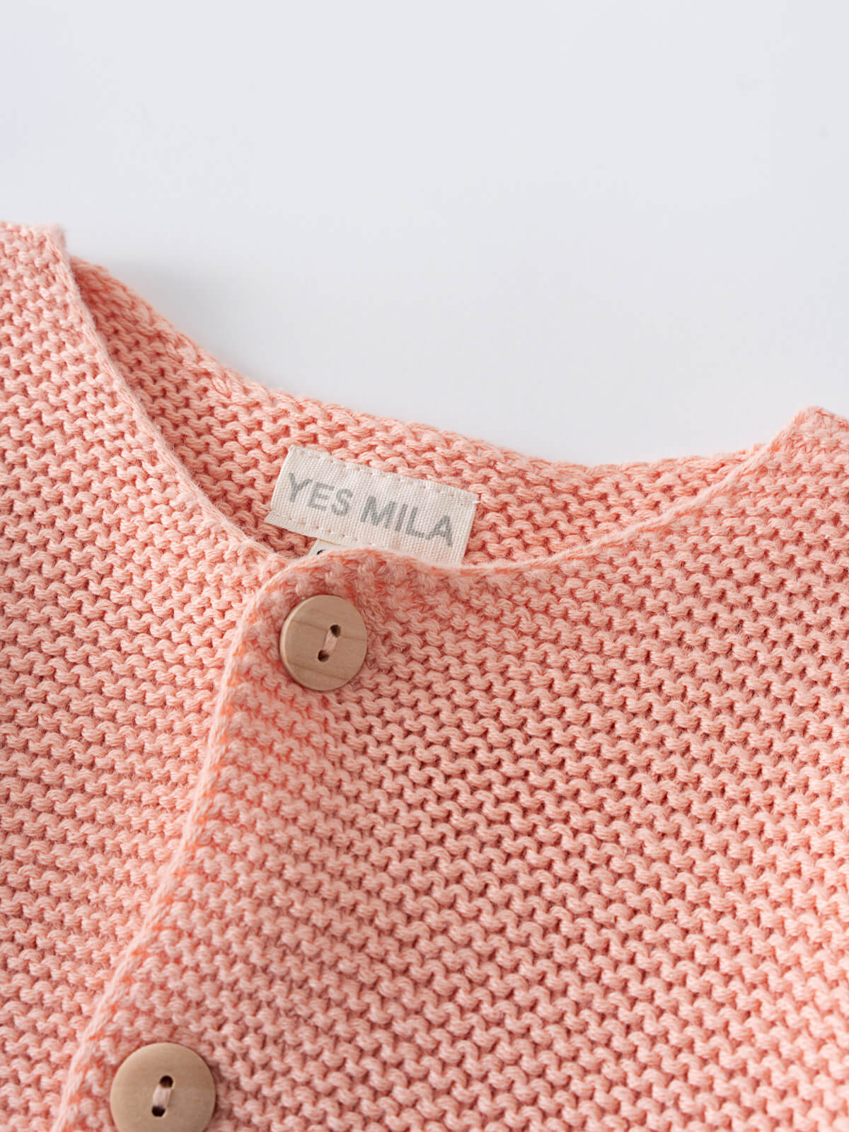 Close-up of a coral pink knitted cardigan with wooden buttons and label Cotton Cardigan - Toasted Peach Baby girl