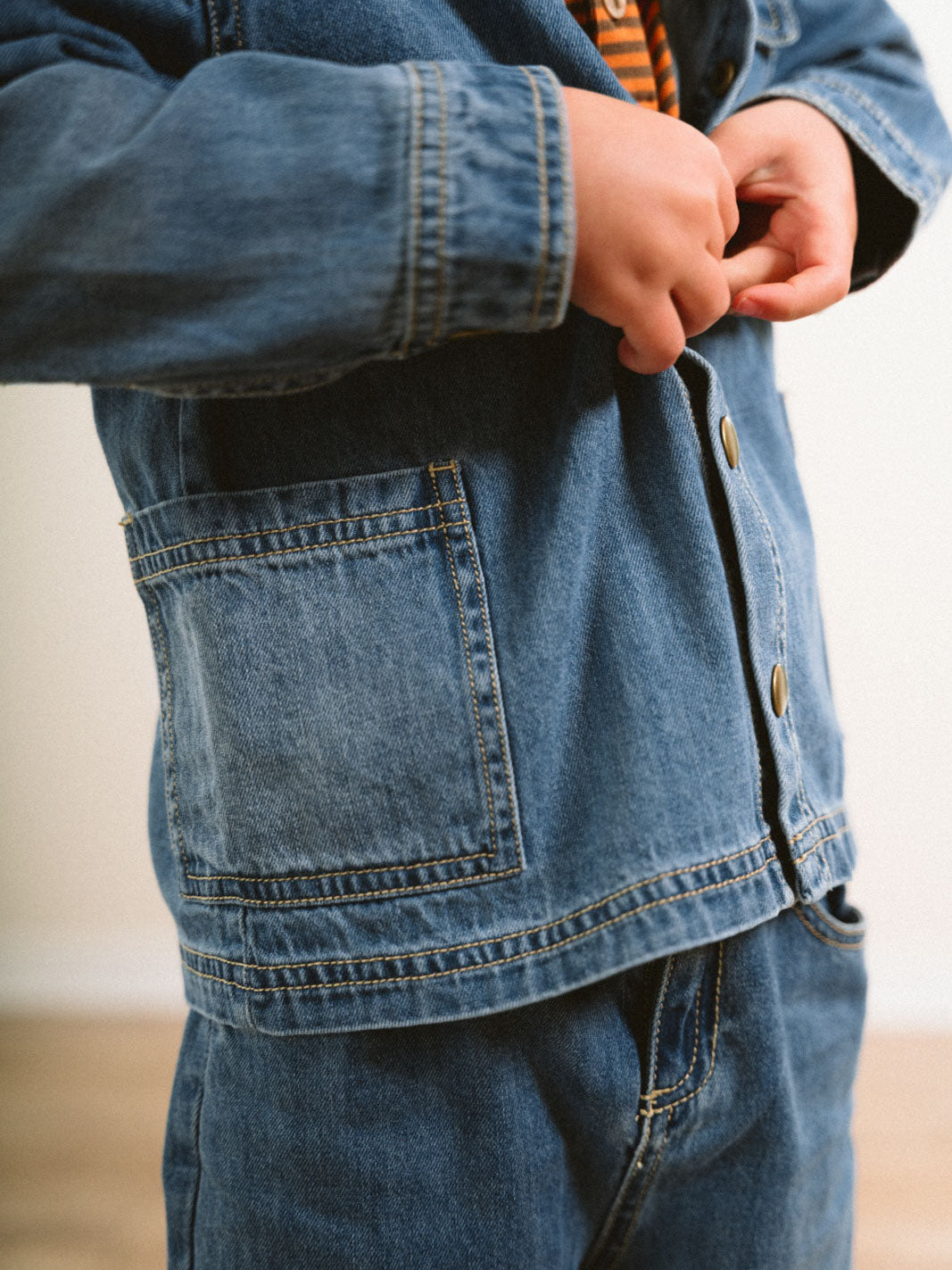 Child wearing denim jacket with hands adjusting belt, showing back pocket detail Denim Jacket - Blue Denim Girls and Boys