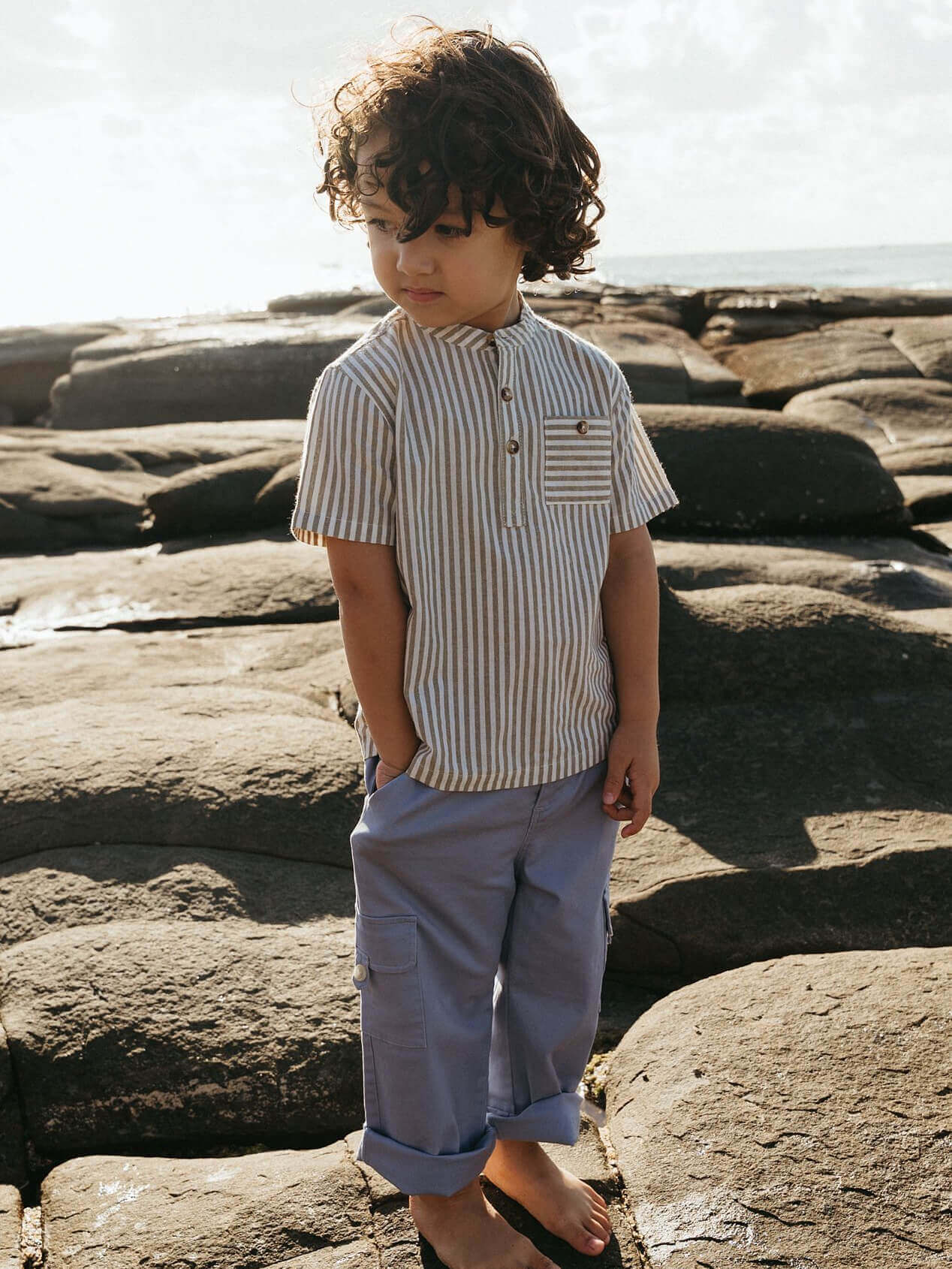 Child wearing a striped shirt and light pants standing on rocks with a natural background