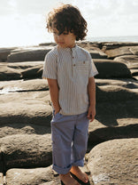 Child wearing a striped shirt and light pants standing on rocks with a natural background