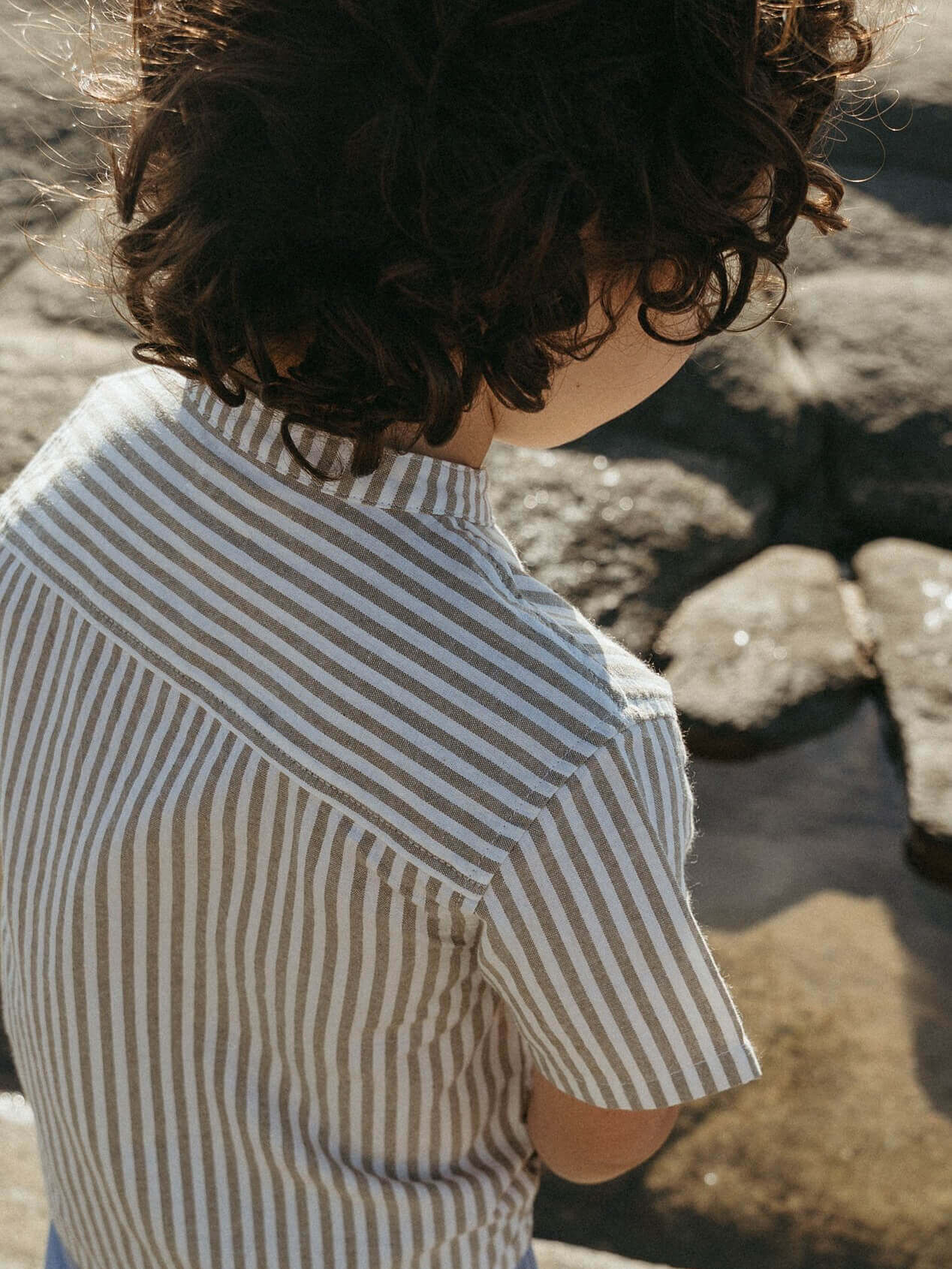 Child wearing a striped shirt standing near water and rocks