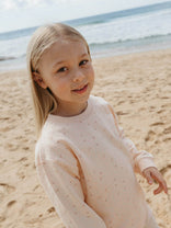 Young girl in a light pink sweater standing on a sandy beach with ocean in the background