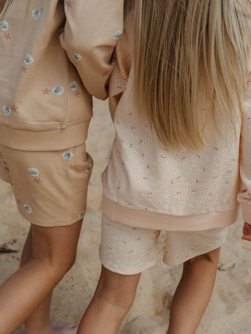 Two children in matching outfits standing close together on a sandy surface.