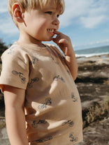 Child wearing a beige shirt with bicycle patterns at the beach