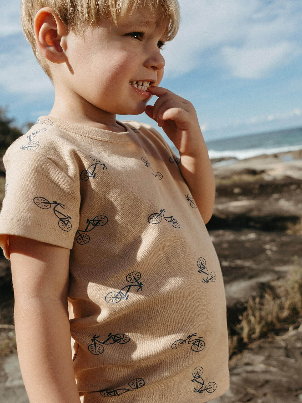 Child wearing a beige shirt with bicycle patterns at the beach