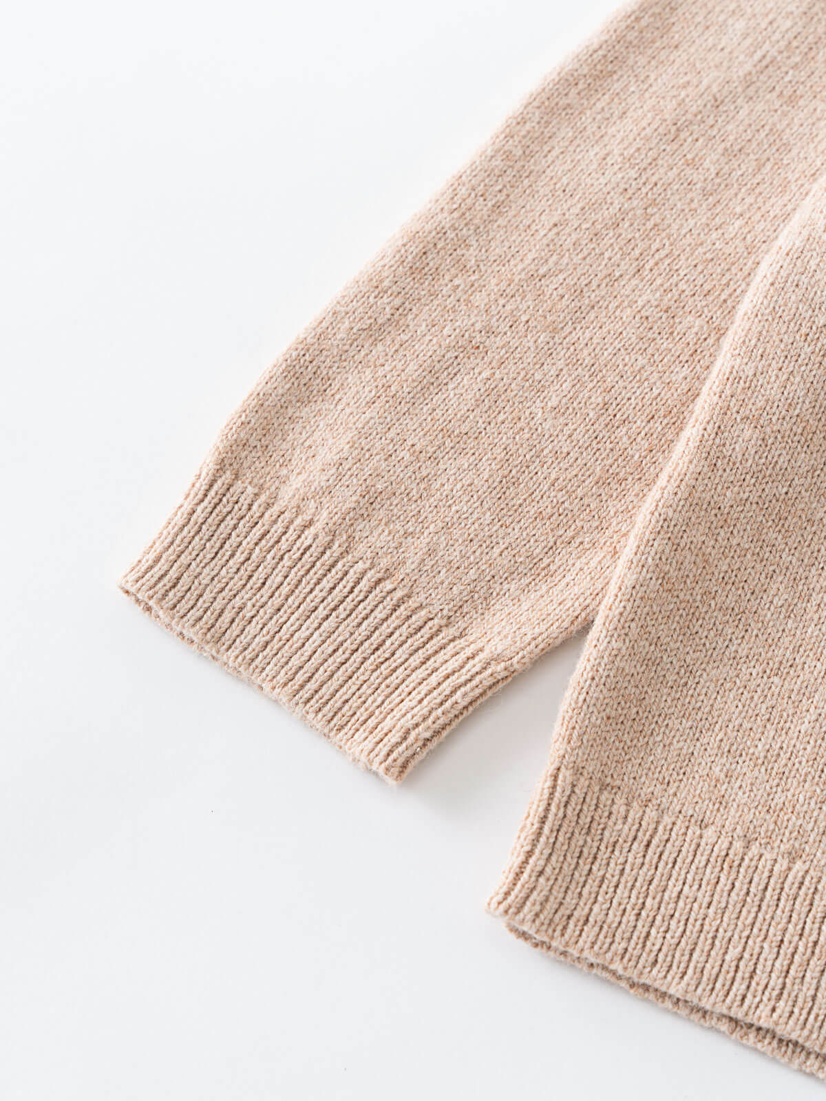 Close-up of a beige knitted sweater sleeve on a white background