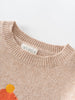 Close-up of a beige sweater with a floral design and 'YES MILA' label on a white background