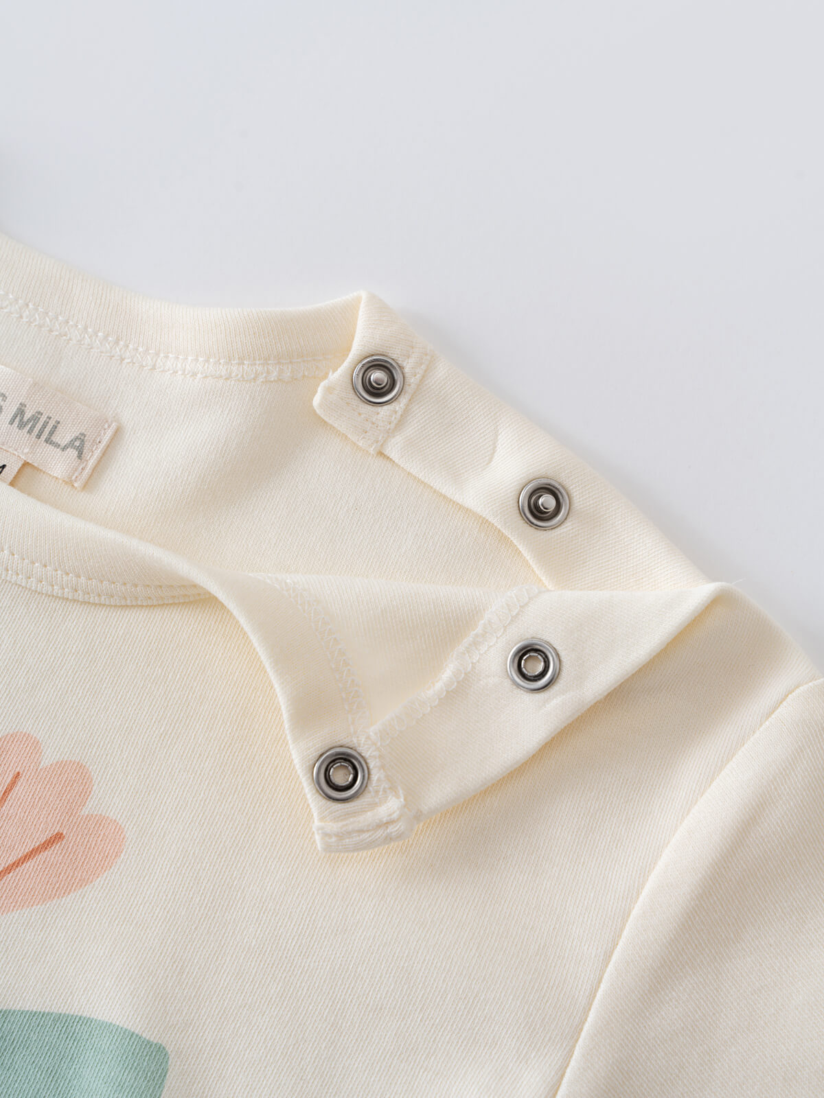Close-up of cream-colored baby garment shoulder with metal snap buttons Feature Print Short Sleeve Tee - Angel Fish Baby girl