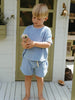 Child in light blue outfit holding a small plant on a wooden deck.